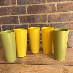 Puede incluir: Cinco vasos de plástico, dos son amarillos y tres son verdes. Los vasos están dispuestos en una fila sobre una superficie de madera.