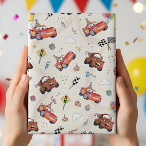 K&ouml;nnte beinhalten: Ein Geschenk, verpackt in gemustertem Papier mit Cartoon-Autos, Partyh&uuml;ten und festlichen Elementen wie Konfetti, Luftballons und Schachflaggen. Der Hintergrund ist hellbeige. Das Geschenk wird von zwei H&auml;nden gehalten.