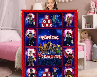 May include: A red-bordered Roblox-themed blanket featuring various character illustrations and the Roblox logo. The blanket has a dark blue background with a grid pattern. The name "Nathan" is also displayed on the blanket.