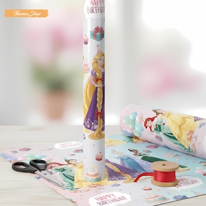 May include: A roll of white wrapping paper featuring a princess design with the text "HAPPY BIRTHDAY". The paper is decorated with images of cakes, gifts, and other princesses. A pair of scissors and a spool of red ribbon are also visible.
