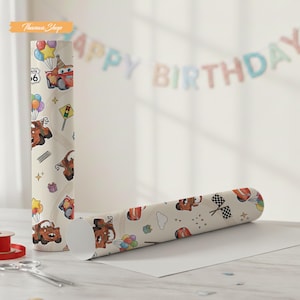 K&ouml;nnte beinhalten: Zwei Rollen Geschenkpapier mit einem sich wiederholenden Muster eines Cartoon-Autos, Luftballons und Verkehrsschildern auf cremefarbenem Hintergrund. Eine Rolle steht aufrecht, die andere liegt. Im Hintergrund steht "Happy Birthday".