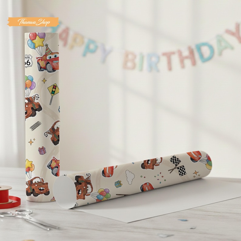 K&ouml;nnte beinhalten: Zwei Rollen Geschenkpapier mit einem sich wiederholenden Muster eines Cartoon-Autos, Luftballons und Verkehrsschildern auf cremefarbenem Hintergrund. Eine Rolle steht aufrecht, die andere liegt. Im Hintergrund steht "Happy Birthday".
