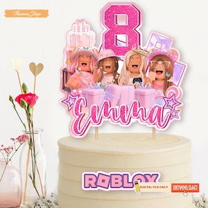 Peut inclure: Un topper de g&acirc;teau rose et blanc avec un chiffre 8 rose, quatre avatars Roblox et le nom "Emma" en lettres scintillantes roses. Le topper de g&acirc;teau est sur un g&acirc;teau blanc avec un logo Roblox rose et blanc.