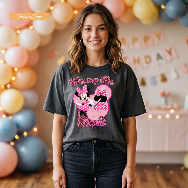 May include: A charcoal gray short-sleeve t-shirt featuring a graphic of Minnie Mouse, the number 2, and the text Birthday Girl Sophia in pink and white. The design includes a pink polka dot pattern on the number and Minnie Mouse's dress.