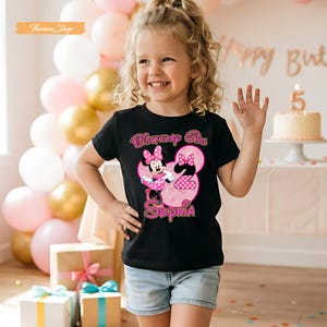 May include: A black short-sleeved t-shirt featuring a graphic of Minnie Mouse, a large pink number two, and the name Sophia in pink lettering. The text Birthday Girl is printed above the character. The design includes pink polka dot accents.