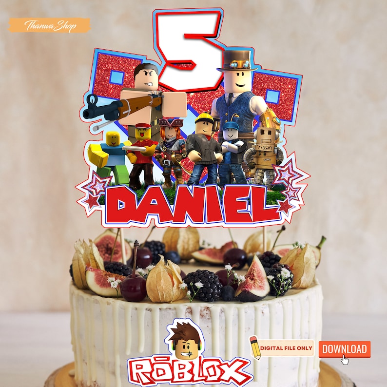 May include: A red, white, and blue cake topper featuring a group of Roblox characters, the number 5, and the name "DANIEL". The cake topper is on top of a white cake decorated with fruit and berries. The cake is on a wooden surface. The text "Roblox" is printed on the cake.