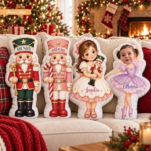 May include: Four custom-shaped plush pillows featuring holiday-themed illustrations. The first is a red and green nutcracker labeled Henry, the second a pink nutcracker labeled Olivia, the third a girl holding a nutcracker labeled Sophia, and the fourth a girl in a purple tutu labeled Aurora.