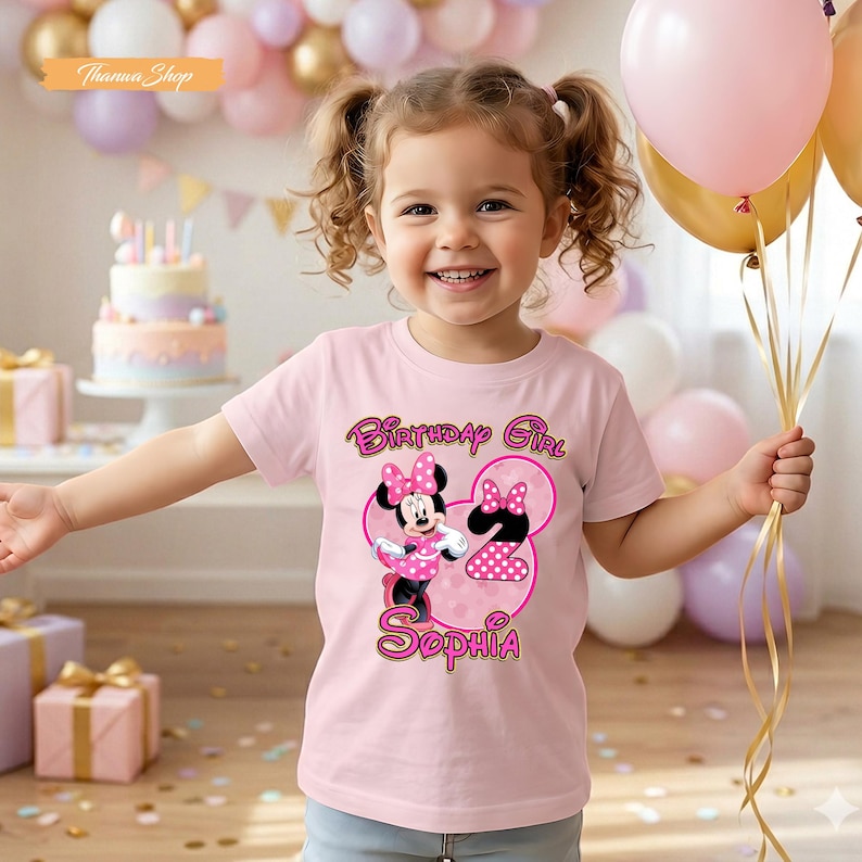 May include: A light pink t-shirt featuring a graphic of Minnie Mouse, the number 2, and the text Birthday Girl Sophia. The design includes pink polka dots and a bow motif. The shirt is worn in a setting with balloons and a birthday cake.