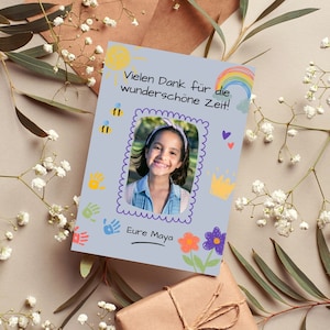 May include: A light blue card with a hand-drawn design featuring a sun, rainbow, bees, flowers, and handprints. The card has a photo of a young girl with a smile and a message that says "Vielen Dank f&uuml;r die wundersch&ouml;ne Zeit!" and "Eure Maya".