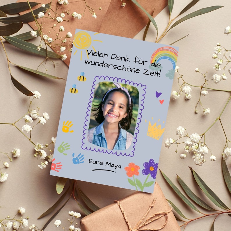 May include: A light blue card with a hand-drawn design featuring a sun, rainbow, bees, flowers, and handprints. The card has a photo of a young girl with a smile and a message that says "Vielen Dank f&uuml;r die wundersch&ouml;ne Zeit!" and "Eure Maya".