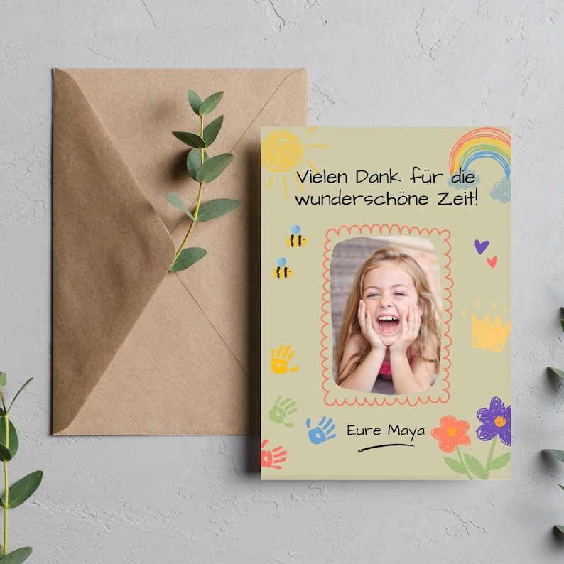 May include: A light green card with a photo of a young girl smiling. The card has a rainbow, sun, bees, handprints, and flowers drawn on it. The text on the card reads "Vielen Dank f&uuml;r die wundersch&ouml;ne Zeit!" and "Eure Maya".