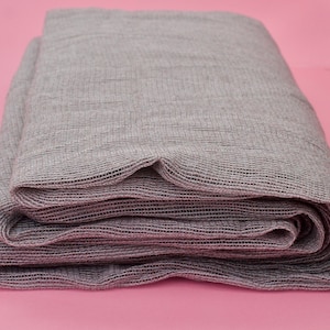 Może przedstawiać: Szara, tkana siatka z tkaniny jest złożona i zwinięta. Tkanina ma miękki, fakturowany wygląd.