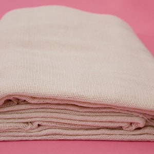 Może przedstawiać: Złożona biała bawełniana serweta, lekka tkanina często używana do cedzenia płynów lub przykrywania żywności.