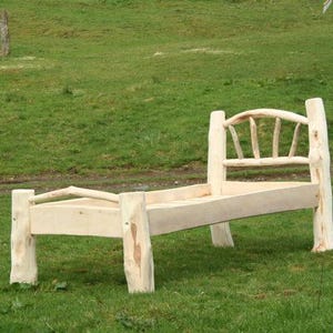 May include: A handcrafted wooden bed frame, constructed from natural logs, with a headboard featuring a curved top and vertical slats. The bed is positioned on a grassy field, showcasing a rustic, unfinished design. The bed's dimensions are in centimeters.