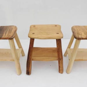 May include: Three wooden stools with a shelf. The stools are made of natural wood with a rustic finish. The stools are all different sizes and shapes.
