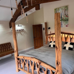 May include: A rustic wooden bed frame with a grey linen headboard and a grey linen duvet. The bed frame is made of natural branches and has a unique, organic design. The bed is decorated with two black and white patterned pillows.