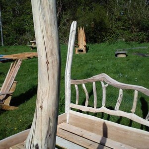 May include: A rustic wooden bed frame with a unique design. The bed features a headboard and footboard made from natural wood branches and a wooden platform. The bed is set outdoors on a grassy area.