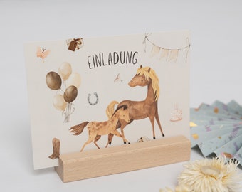 Puede incluir: Una tarjeta blanca con un caballo marrón y un potro marrón en ella. La tarjeta dice "Einladung", que en alemán significa "Invitación". La tarjeta está en un soporte de madera.