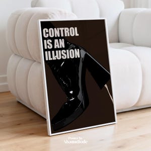 Könnte beinhalten: Ein gerahmtes Poster mit dem Text "CONTROL IS AN ILLUSION" in Weiß. Das Poster zeigt einen schwarzen, glänzenden Stiefel und ein Bein vor einem dunkelbraunen Hintergrund. Das Poster wird auf einem Holzboden neben einem weißen Sofa angezeigt.