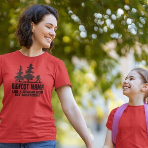 A red t-shirt with black text that reads 'BIGFOOT MAMA LIKE A REGULAR MOM BUT SQUATCHIER' and a graphic of a Bigfoot walking in front of two trees.