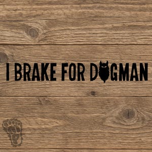 May include: A wooden sign with the phrase "I Brake for Dogman" in black lettering. The word "Dogman" features a silhouette of a dog's head. A paw print is in the lower left corner. The background is a wood grain pattern.