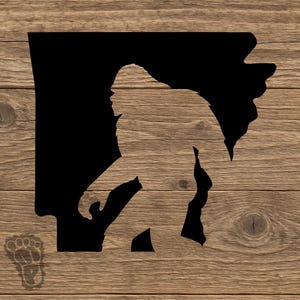 May include: A wooden sign featuring a silhouette of Bigfoot within the outline of the state of Arkansas. The sign has a natural wood grain background and a Bigfoot footprint in the lower left corner.