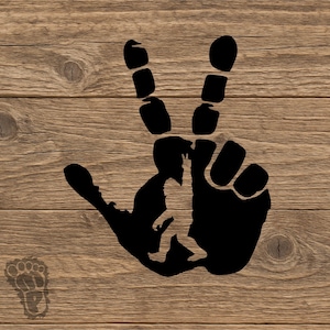 May include: Black hand silhouette forming a peace sign with a Bigfoot silhouette in the center. The background is a wooden texture. A Bigfoot footprint is in the lower left corner.