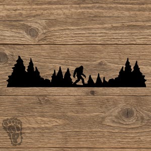 May include: A black silhouette decal featuring a Bigfoot figure walking through a dense forest of pine trees. In the lower left corner, there is a small, faint outline of a footprint shape with the letter P inside it, set against a wood grain background.
