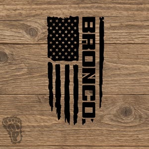 May include: A black graphic design featuring a stylized American flag with a distressed, vertical orientation. The word BRONCO is printed in bold, black, capital letters vertically along the right side of the flag design.