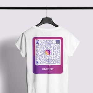 Op de afbeelding: Wit T-shirt met een QR-code ontwerp op de achterkant. De QR-code staat in een paars en roze gradiënt rechthoek, met het Instagram logo. De tekst "YOUR TEXT" staat eronder.