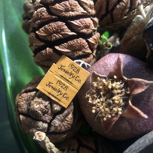 May include: Two brown pine cones and a dark purple dried pomegranate with a small brown tag that reads "1928 Jewelry Co."