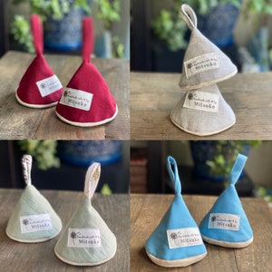 May include: A collection of handmade pot holders in various colors, including red, gray, green, and blue. Each pot holder has a loop for hanging and a label that reads "handmade with love by Mitsuko."