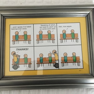 以下が含まれることがあります： 銀色のフレームと黄色のマットが付いた額入りの漫画。漫画は、吹き出しのあるパネルに棒人間を描いています。テキストには、「...and I guess I've hated ketchup ever since」や「THANKS！」などのフレーズが含まれています。