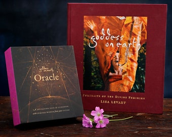 Può includere: Un set di carte di oracoli in una scatola con un design nero e oro e il testo "goddess on earth Oracle" sul davanti. La scatola è accanto a un libro con una copertina rossa e il testo "goddess on earth Portraits of the Divine Feminine Lisa Levart" sul davanti.