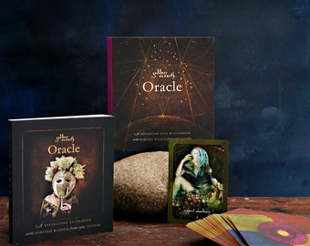 May include: A set of oracle cards with a guidebook. The guidebook has a dark background with a woman wearing a mask and a floral crown. The cards have a gold background with a woman sitting on a rock. The text on the guidebook reads "Goddess in Earth Oracle" and "A Divination Guidebook with Spirited Wisdom from your Sisters". The text on the cards reads "Expect Abundance".