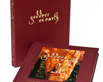 Può includere: Un libro rilegato in bordeaux dal titolo "goddess on earth: Portraits of the Divine Feminine" di Lisa Levart. Il libro è chiuso e la copertina presenta una foto di una donna con le braccia alzate, che indossa una sciarpa arancione fluttuante.