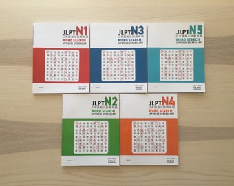 Könnte beinhalten: Fünf unterschiedlich farbige Bücher mit dem Titel "JLPT N1, N2, N3, N4, N5" und den Worten "Wortsuche Japanisches Vokabular" auf dem Cover. Die Bücher sind in einer Reihe von links nach rechts angeordnet, wobei das N1-Buch links und das N5-Buch rechts ist.