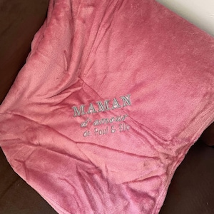 Peut inclure: Une couverture en polaire rose avec le texte "MAMAN d'amour de Paul & Elle" brodé en gris.