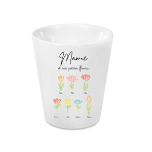 Peut inclure: Gobelet en céramique blanc avec le texte "Mamie et ses petites fleurs" et des illustrations de fleurs colorées. Le gobelet a un design simple et élégant, parfait pour un usage quotidien.