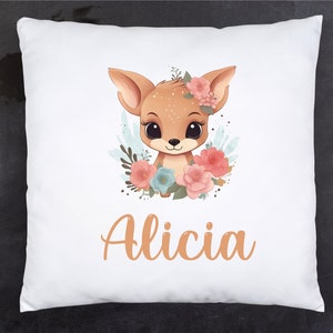 Peut inclure: Un oreiller blanc avec un adorable cerf de dessin animé avec des fleurs roses et bleues et le nom Alicia en orange.