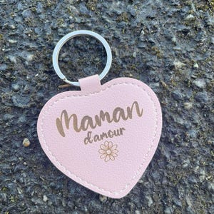 May include: Pink leather heart-shaped keychain with a gold inscription that reads "Maman d'amour" and a small gold flower design.