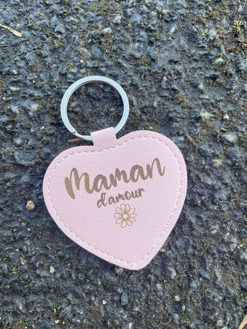 May include: Pink leather heart-shaped keychain with a gold inscription that reads "Maman d'amour" and a small gold flower design.