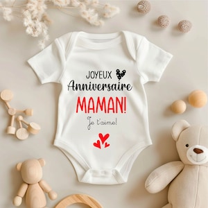 May include: White baby onesie with black text that reads "Joyeux Anniversaire Maman! Je t'aime!" with a black and white polka dot heart and three red hearts.