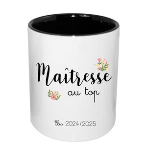 Peut inclure: Mug en céramique blanche avec intérieur noir. Il porte l'inscription "Maîtresse au top" en écriture noire, avec des motifs floraux. Le nom "Elio 2024/2025" est imprimé en bas. Idéal pour un cadeau.