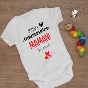 May include: White baby onesie with black text that reads "Joyeux Anniversaire Maman! Je t'aime!" with red hearts.