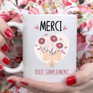 Peut inclure: Mug en céramique blanche avec un motif floral rose et jaune et le texte "MERCI TOUT SIMPLEMENT..." en noir.