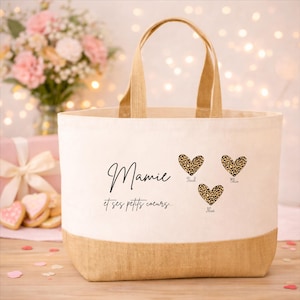 K&ouml;nnte beinhalten: Cremefarbene Tragetasche mit einem Boden und Griffen aus nat&uuml;rlichem Jute. Die Tasche hat das Wort "Mamie" in Schreibschrift, mit drei Leopardenherzen und dem Text "et ses petits coeurs".