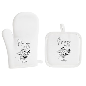 May include: White oven mitt and square pot holder set. Both items feature the text "Nounou en Or" and "de L&eacute;on" in black script, along with a floral design. The mitt has a loop for hanging.