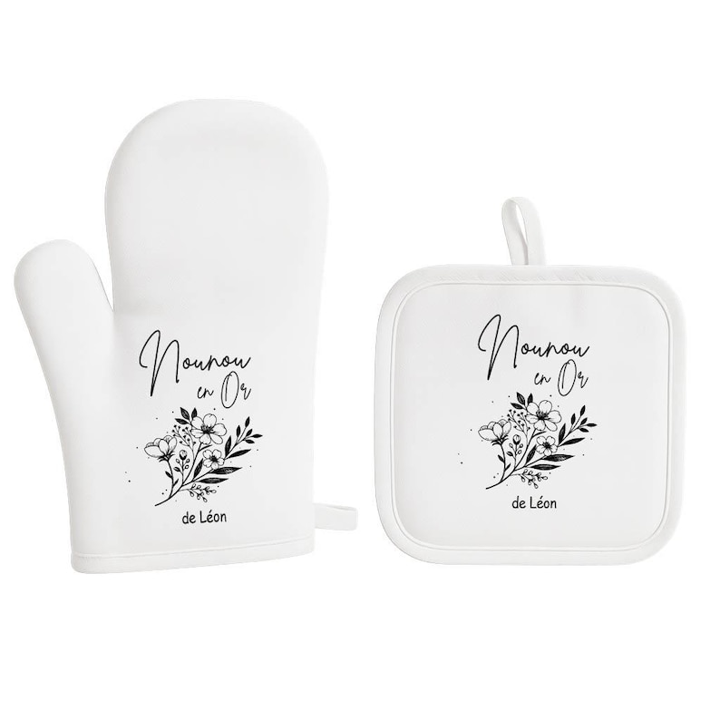 May include: White oven mitt and square pot holder set. Both items feature the text "Nounou en Or" and "de L&eacute;on" in black script, along with a floral design. The mitt has a loop for hanging.