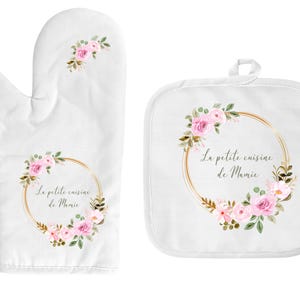 Peut inclure: Deux maniques de cuisine blanches avec un motif floral et une inscription dorée. Le texte dit "La petite cuisine de Mamie".